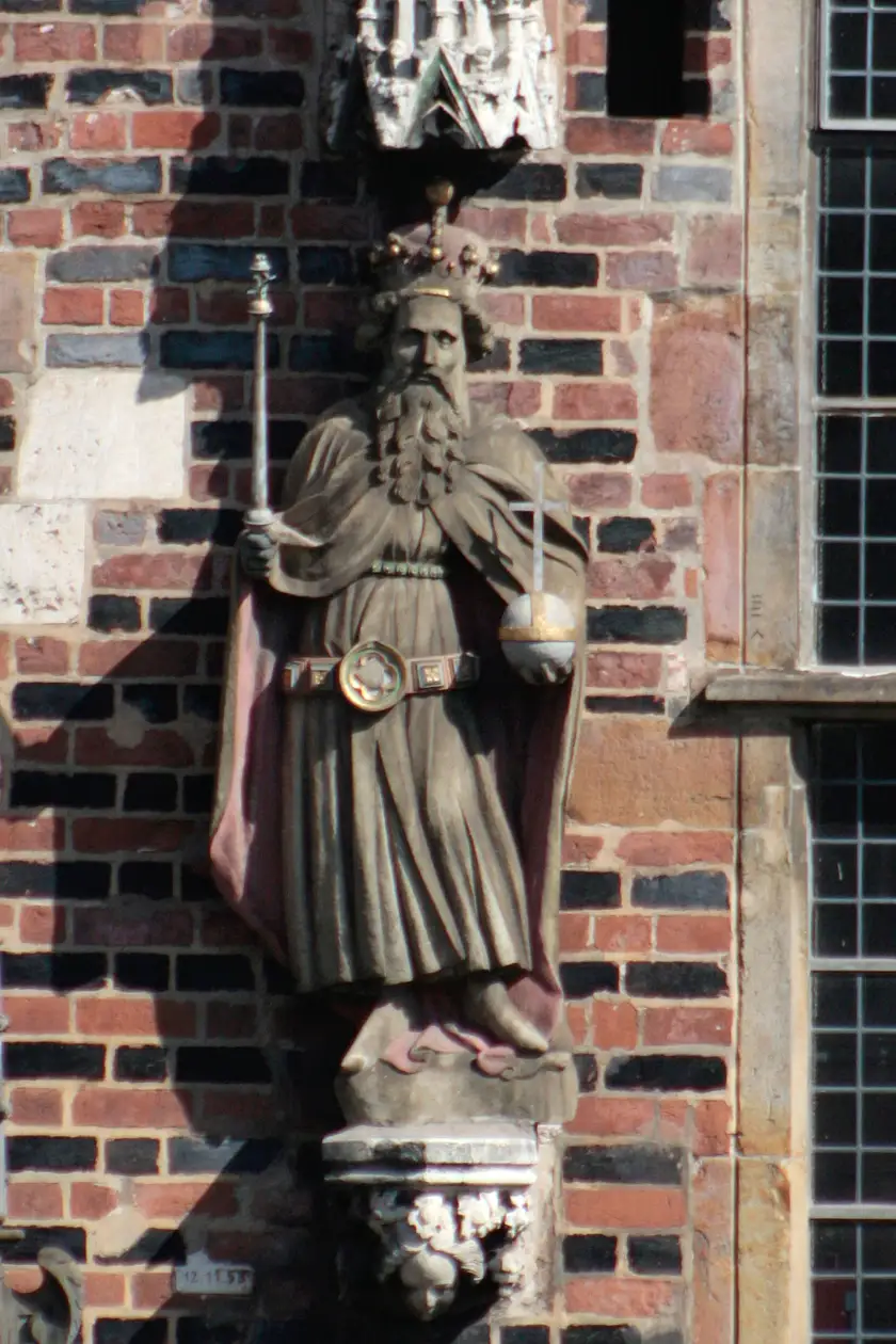 Der Kaiser ist mit drei besonderen Machtsymbolen, den Insignien des Monarchen, ausgestattet. Er trägt in der linken Hand den Reichsapfel, in der Rechten hält er das Zepter und auf dem Haupt trägt er die Krone. Anders als die Kurfürsten hält er keine Waffe in der Hand und trägt auch keine Handschuhe. Gekleidet ist er in ein knöchellanges Gewand.