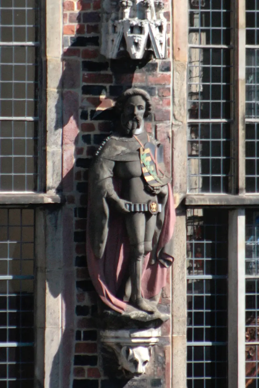 Zwar zeigt die ebenfalls in einen Mantel gehüllte Figur des Kurfürst von Sachsen keine Waffen, es gibt jedoch Brustpanzer, Beinschienen und Kacheln an den Knien. Sein Gewand wird gehalten von einem Dupfing, der einen Vogel auf der Schnalle hat.