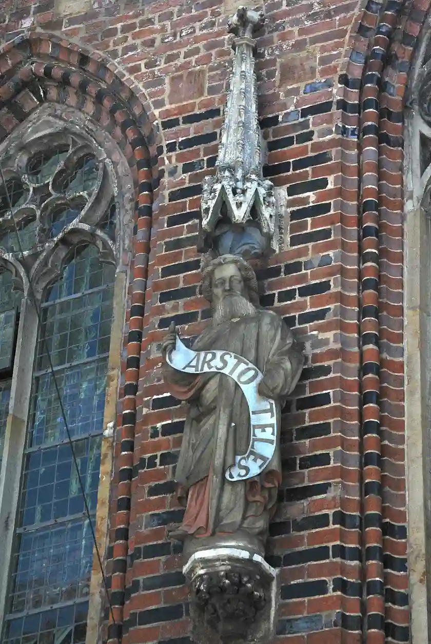 Die durch das Spruchband als Aristoteles gekennzeichnete Figur - ursprünglich Prophet Jeremia - hält dieses mit beiden Händen fest, wobei die linke Hand durch sein Gewand verdeckt ist.