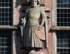 Der Kurfürst von Mainz kann anhand des Wappens auf seinem Schilde, dem sechsspeichigen Rad, identifiziert werden. Außerdem trägt er ein Schwert. Bekleidet ist er mit einem Wams und einem faltigen Rock. Über der Schulter trägt er eine Kapuze.