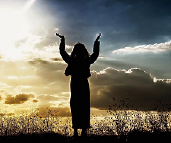 Symbolbild für Religionsangelegenheiten. Eine Frau steht auf einer Wiese und hält ihre Hände Richtung Himmel hoch.