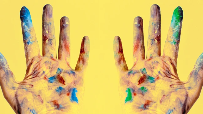 Symbolbild für Kunst. Man sieht zwei angemalte Hände auf einem gelben Hintergrund.